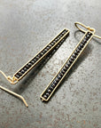 This image displays a pair of sophisticated Black Diamond Beaded Stick Earrings. The earrings feature long, slender 14k gold-frames, each adorned with a series of small black beads.