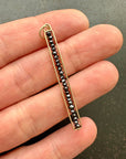 Gold pendant with black beads held between fingers on a dark surface
