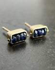 Pair of gold stud earrings with blue sapphire beads on a dark surface
