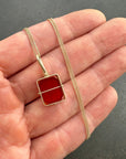 Gold necklace with a carnelian pendant held in a hand against a gray background
