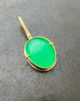 An oval pendant featuring a vibrant green chrysoprase gemstone in a gold bezel setting with a gold hook, displayed on a textured dark gray background.