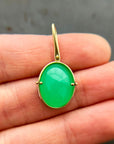An oval pendant featuring a vibrant green chrysoprase gemstone in a gold bezel setting with a gold hook, displayed on a hand.