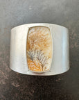 Silver cuff bracelet with a dendritic agate stone inlay on a gray surface