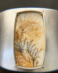 Silver cuff bracelet with a dendritic agate stone inlay on a gray surface