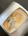 Silver cuff bracelet with a dendritic agate stone inlay on a gray surface