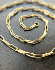 An 18k gold elongated oval chain necklace coiled in a spiral on a textured gray surface.