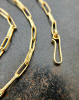 An 18k gold elongated oval chain necklace coiled in a spiral on a textured gray surface.