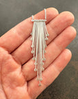 Silver fringe necklace held in a hand against a dark background