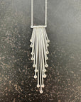 Silver necklace with dangling fringe on a gray surface