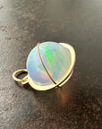 Opal orb pendant in a gold setting on a dark surface