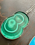 Green malachite pendant on a chain against a textured brown background