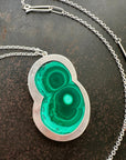 Necklace with a green malachite and silver pendant on a dark surface