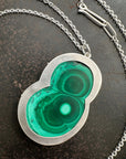 Necklace with a green malachite and silver pendant on a dark surface