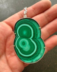 Green malachite pendant held in a hand against a dark background