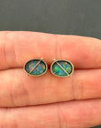 Opal stud earrings held between two fingers against a dark background