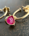 14k Gold hoop earrings with a bright pink ruby gemstone hoop charm, shown close up on a dark textured surface.