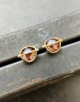 Pair of gold stud earrings with rustic diamond on a dark surface