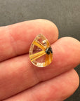 A teardrop-shaped gemstone featuring a striking golden-yellow radial pattern with a small dark inclusions, centered on a hand.