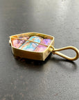 An 18k gold pendant with a loop bale, featuring three wood replacement opals showing purple, blue, and green hues, resting on a dark gray textured surface.