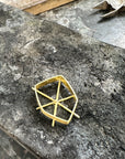 A small gold metal jewelry component or frame piece resting on a dark, textured stone surface with metal tools visible in the background.