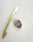 A shield-shaped pendant featuring an 18k gold frame and three rectangular inlay wood replacement opals in pink, turquoise, purple, and brown.