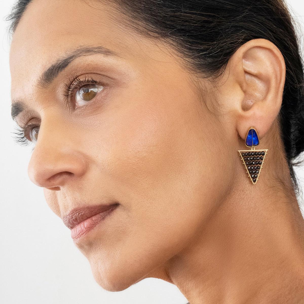 Woman wearing a black diamond triangle earring with a blue opal gemstone on a white background