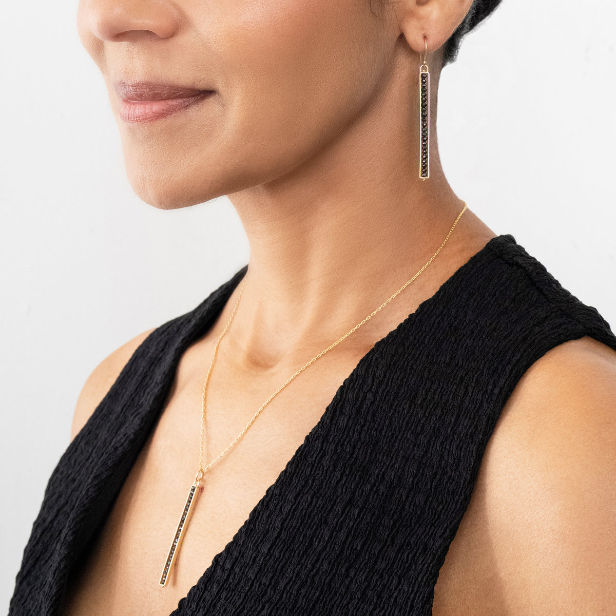 Woman wearing black diamond gold earrings and black diamond gold necklace on a white background