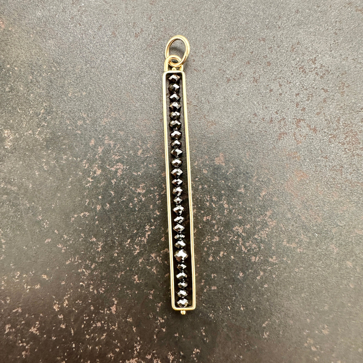 Gold pendant with black diamond beads on a gray surface