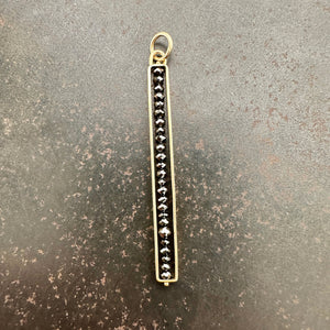 Gold pendant with black diamond beads on a gray surface