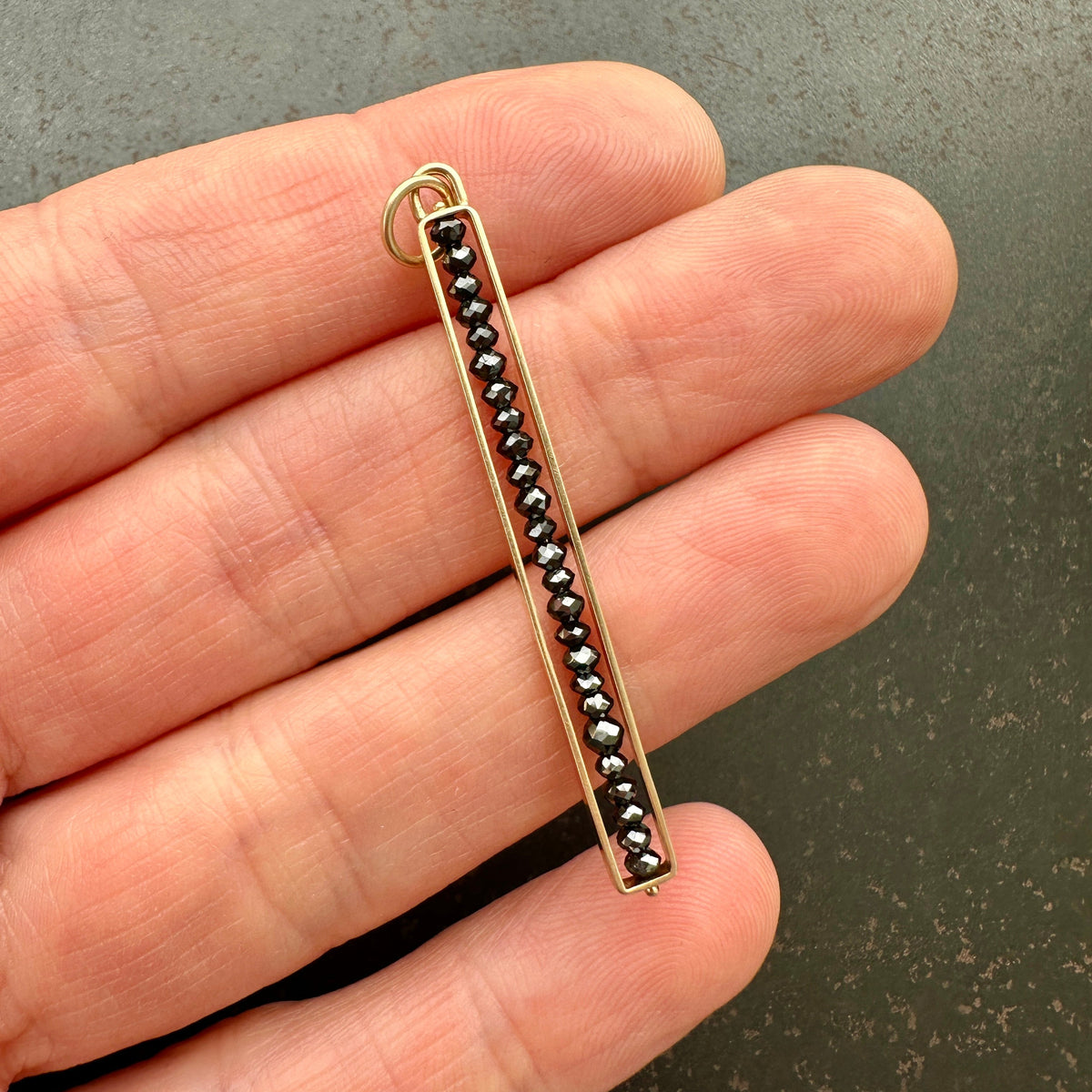 Gold pendant with black beads held between fingers on a dark surface