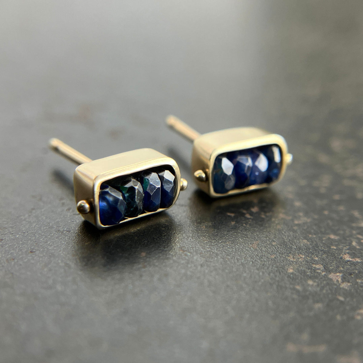 Pair of gold stud earrings with blue sapphire beads on a dark surface
