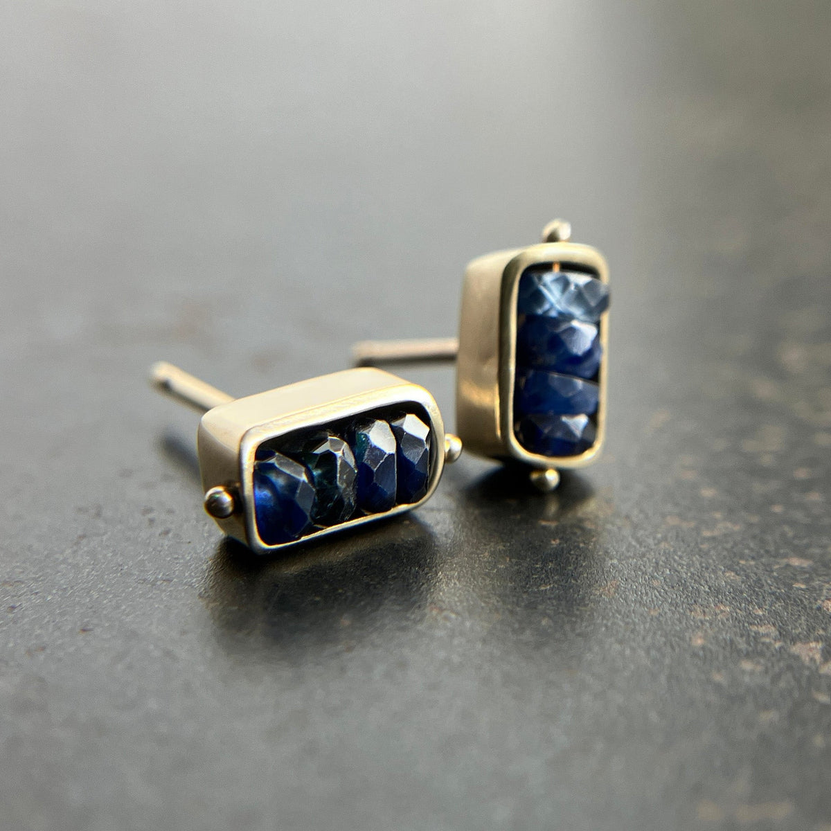 Pair of gold stud earrings with blue sapphire beads on a dark surface