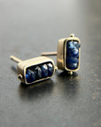 Pair of gold stud earrings with blue sapphire beads on a dark surface