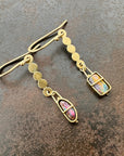 A pair of 18k gold dangle earrings with scalloped circular links and rectangular bezel-set iridescent boulder opal stones, displayed on a textured dark brown surface.