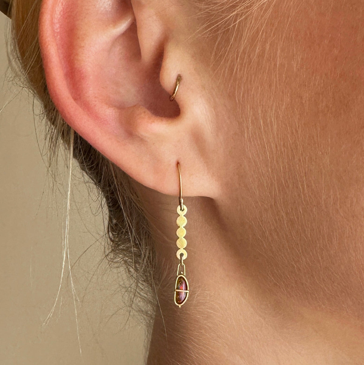 A pair of 18k gold dangle earrings with scalloped circular links and rectangular bezel-set iridescent boulder opal stones, displayed on a model.