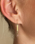 A pair of 18k gold dangle earrings with scalloped circular links and rectangular bezel-set iridescent boulder opal stones, displayed on a model.
