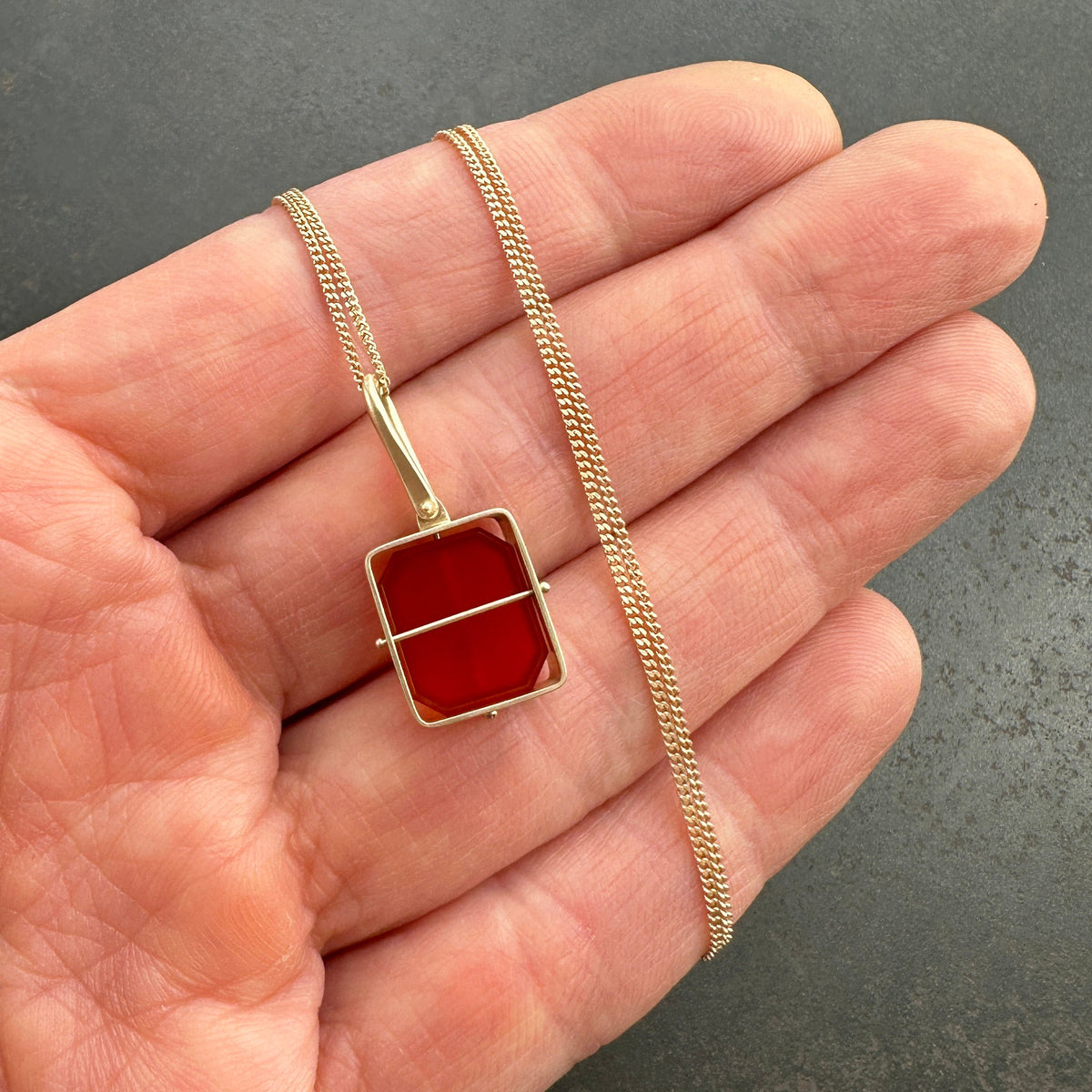 Gold necklace with a carnelian pendant held in a hand against a gray background