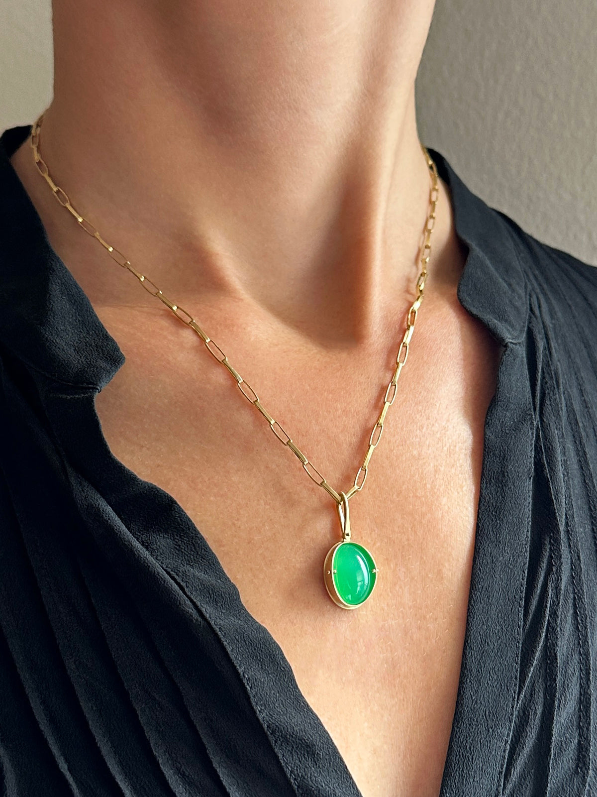 An oval pendant featuring a vibrant green chrysoprase gemstone in a gold bezel setting with a gold hook, displayed on a model.