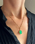 An oval pendant featuring a vibrant green chrysoprase gemstone in a gold bezel setting with a gold hook, displayed on a model.