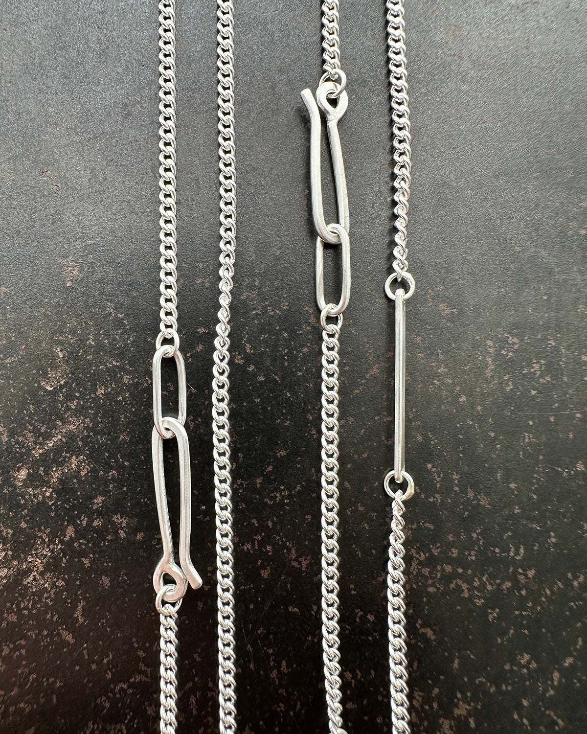 silver curb chains on a dark textured surface