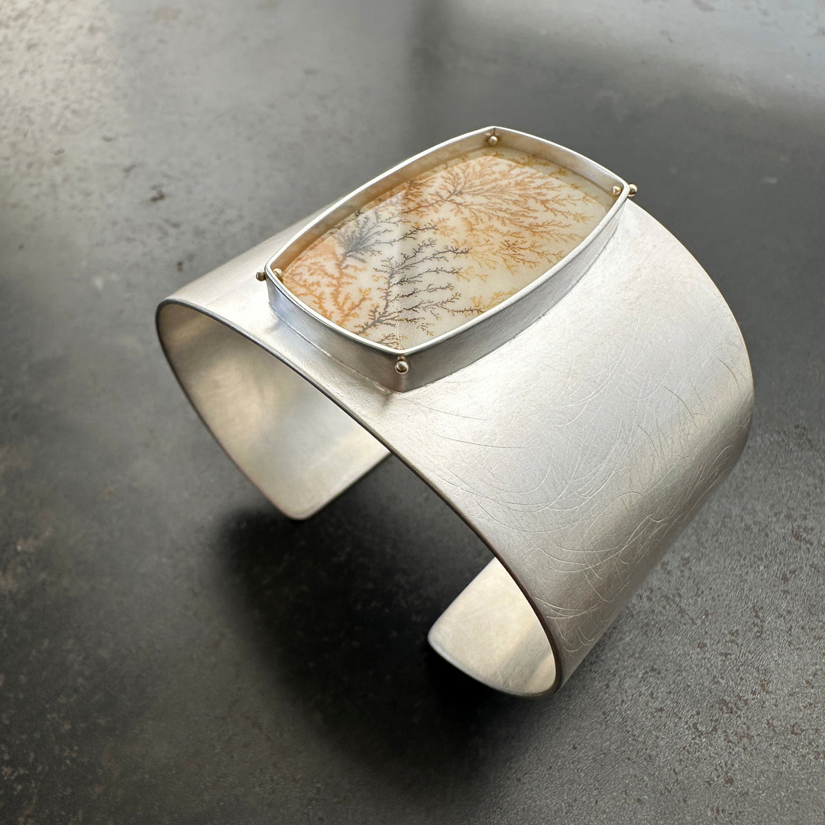 Silver cuff bracelet with a dendritic agate stone inlay on a gray surface