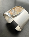 Silver cuff bracelet with a dendritic agate stone inlay on a gray surface