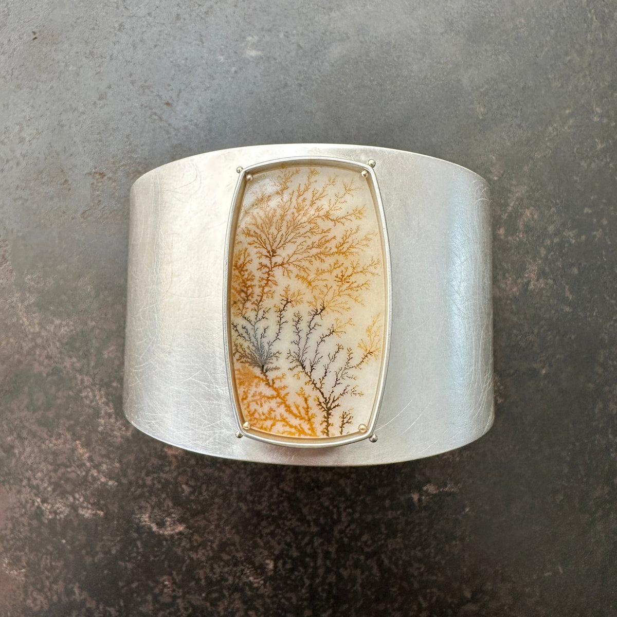 Silver cuff bracelet with a dendritic agate stone inlay on a gray surface