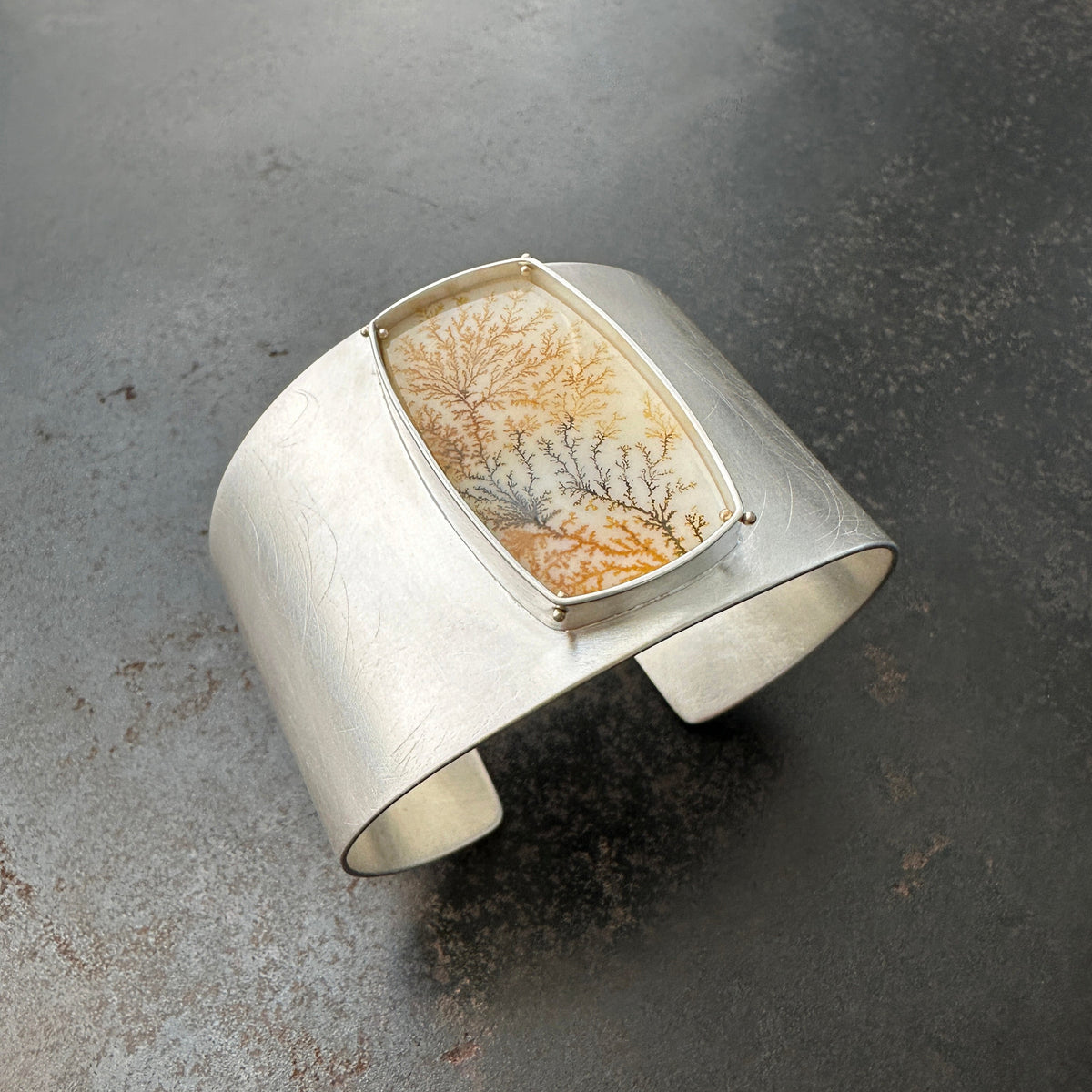 Silver cuff bracelet with a dendritic agate stone inlay on a gray surface