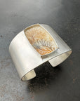 Silver cuff bracelet with a dendritic agate stone inlay on a gray surface