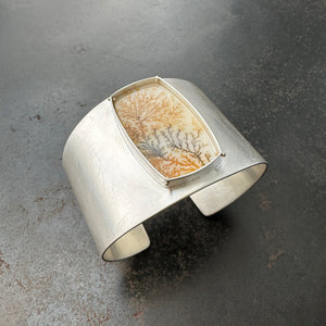 Silver cuff bracelet with a dendritic agate stone inlay on a gray surface