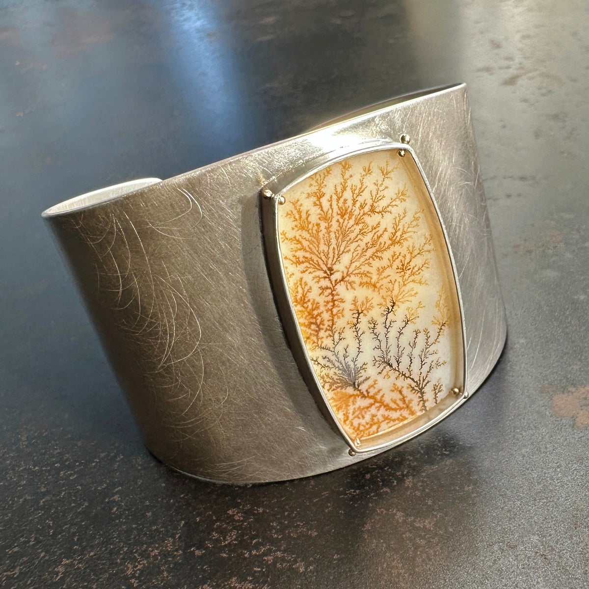 Silver cuff bracelet with a dendritic agate stone inlay on a gray surface