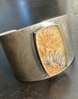 Silver cuff bracelet with a dendritic agate stone inlay on a gray surface
