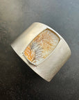 Silver cuff bracelet with a dendritic agate stone inlay on a gray surface