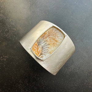 Silver cuff bracelet with a dendritic agate stone inlay on a gray surface